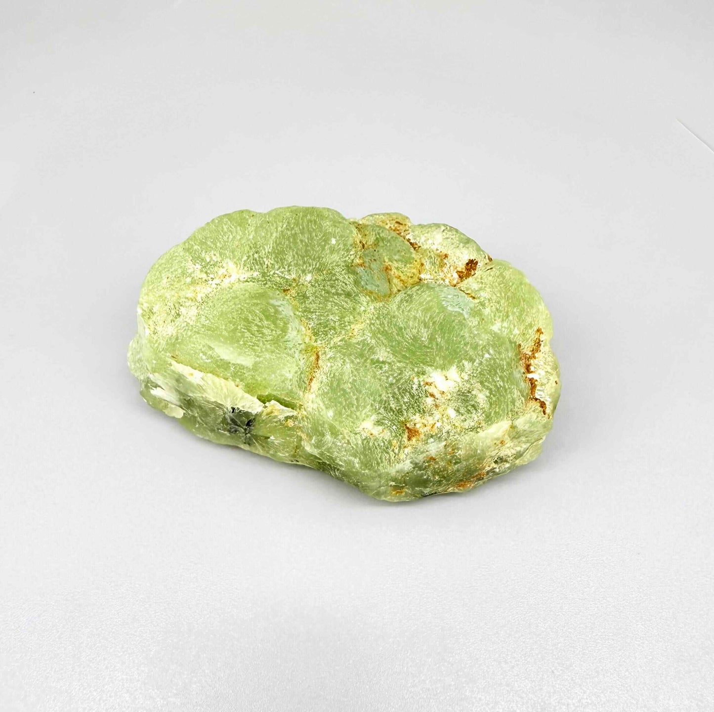 Prehnite rough stone in pale apple-green color with dark inclusions and semi-translucent body.