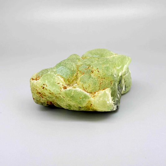 Prehnite rough stone in pale apple-green color with dark inclusions and semi-translucent body.