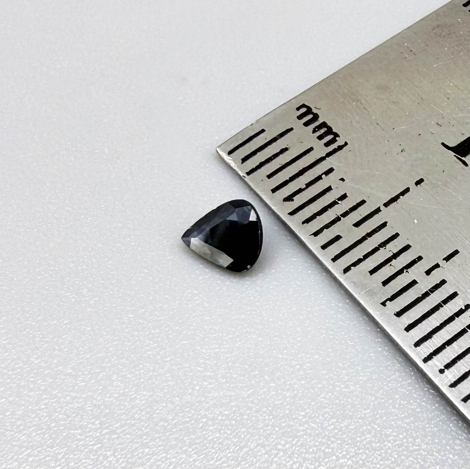 Trillion-cut dark teal blue sapphire from Bangkaja, Thailand, natural faceted gemstone with deep blue-green undertones.
