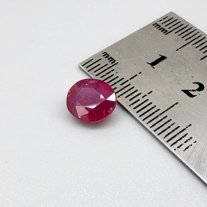 Oval pinkish red ruby from Mozambique with vibrant color, visible natural inclusions and soft, semi-transparent appearance.