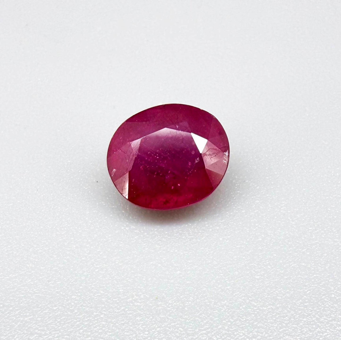 Oval pinkish red ruby from Mozambique with vibrant color, visible natural inclusions and soft, semi-transparent appearance.