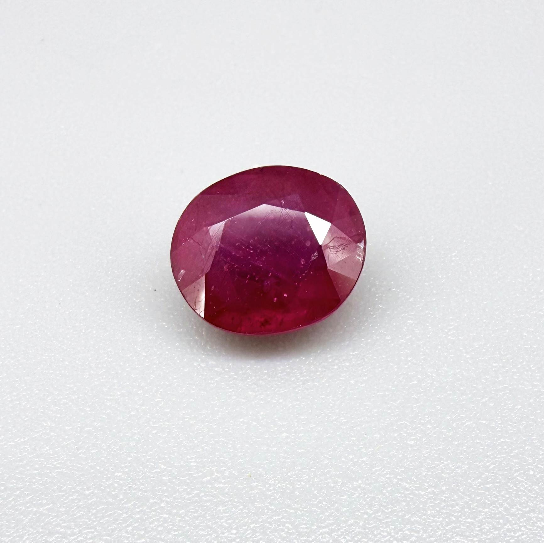 Oval pinkish red ruby from Mozambique with vibrant color, visible natural inclusions and soft, semi-transparent appearance.