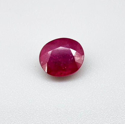 Oval pinkish red ruby from Mozambique with vibrant color, visible natural inclusions and soft, semi-transparent appearance.