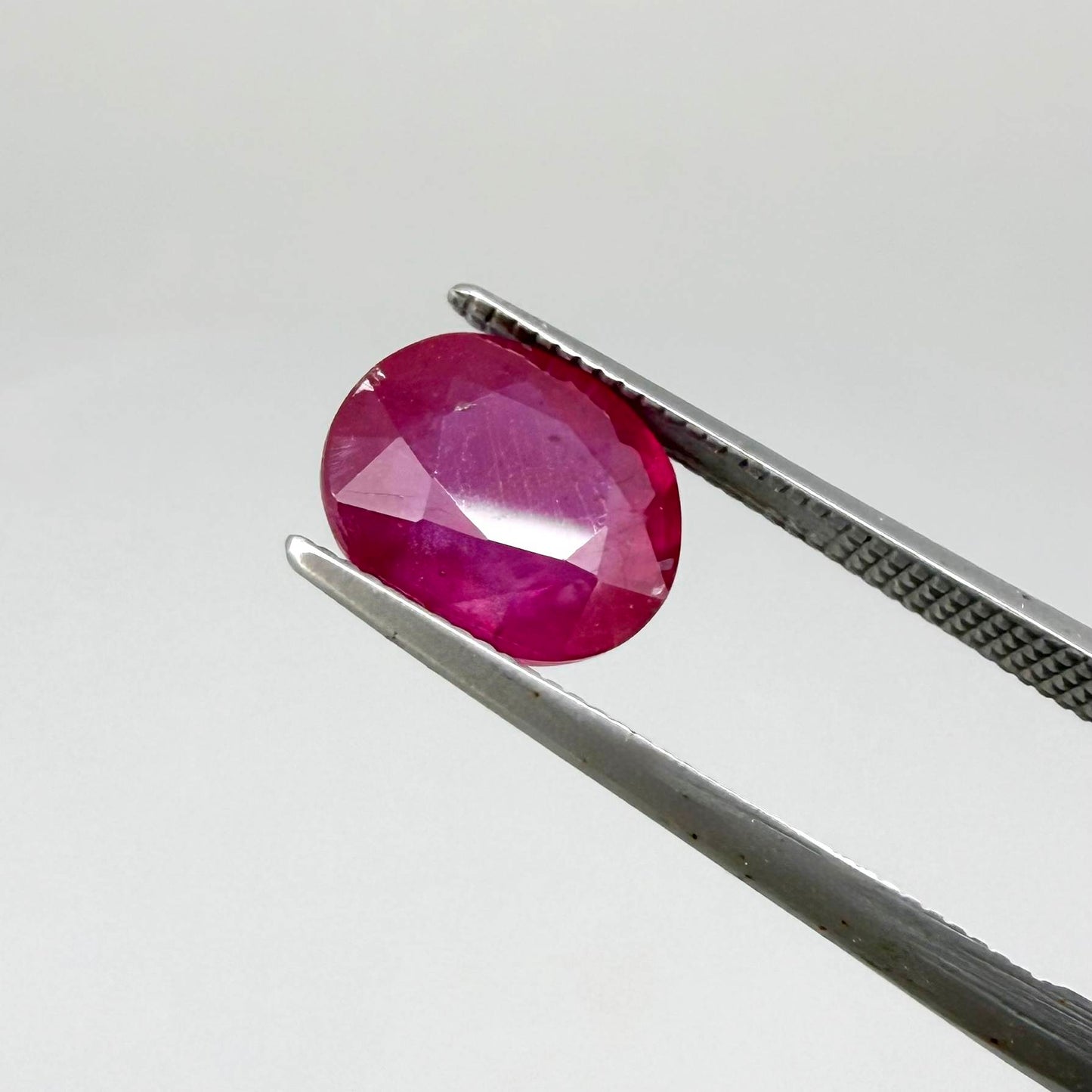 Oval pinkish red ruby from Mozambique with vibrant color, visible natural inclusions and soft, semi-transparent appearance.