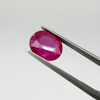 Oval pinkish red ruby from Mozambique with vibrant color, visible natural inclusions and soft, semi-transparent appearance.