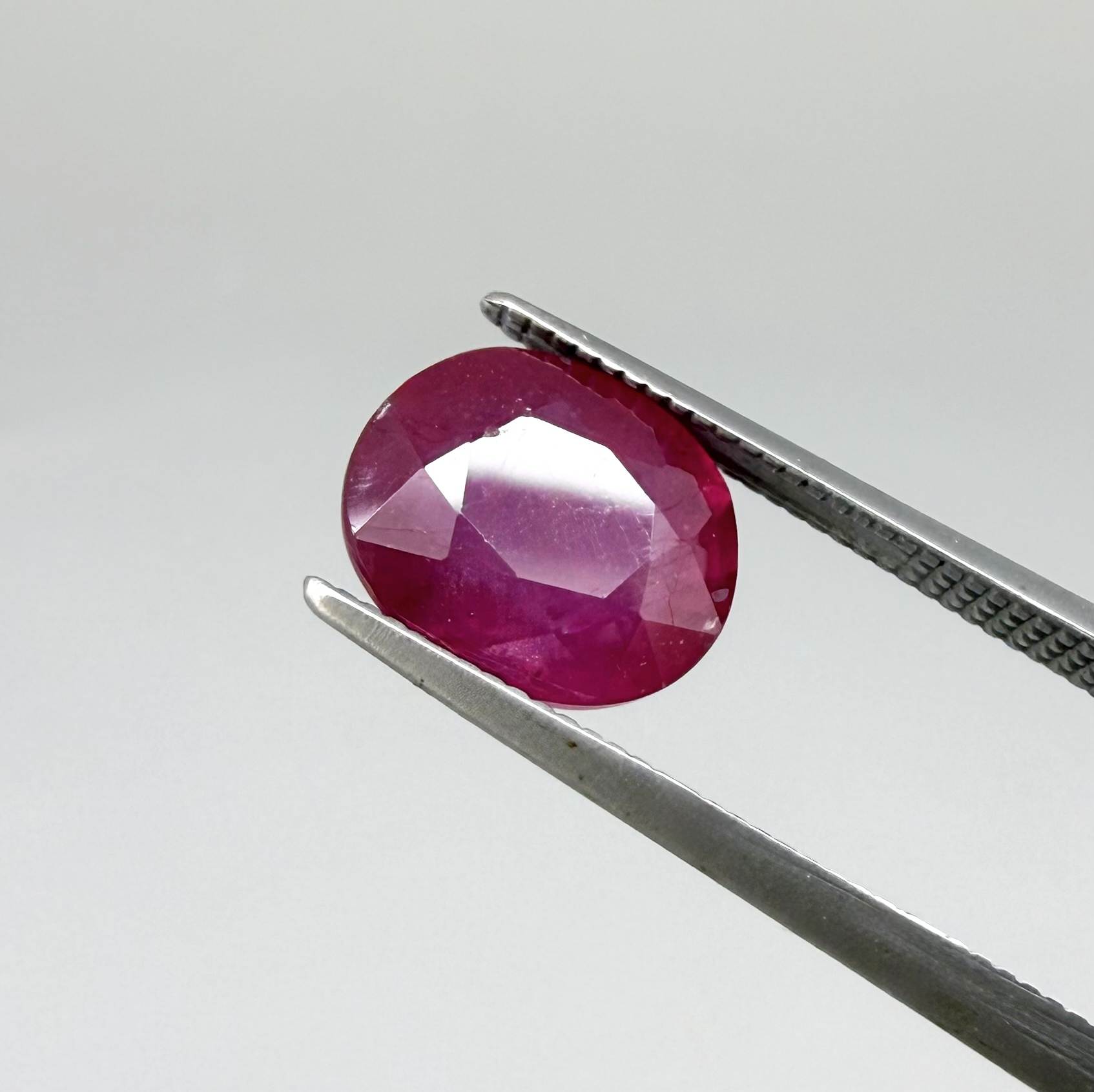 Oval pinkish red ruby from Mozambique with vibrant color, visible natural inclusions and soft, semi-transparent appearance.