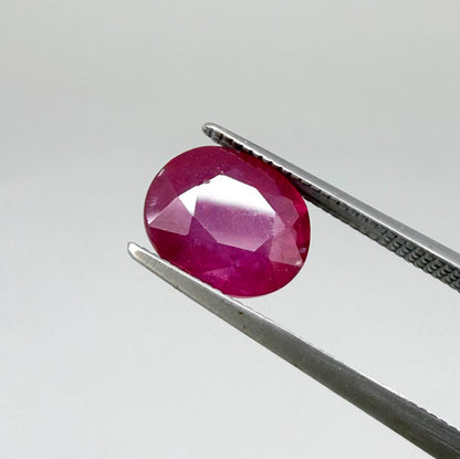 Oval pinkish red ruby from Mozambique with vibrant color, visible natural inclusions and soft, semi-transparent appearance.