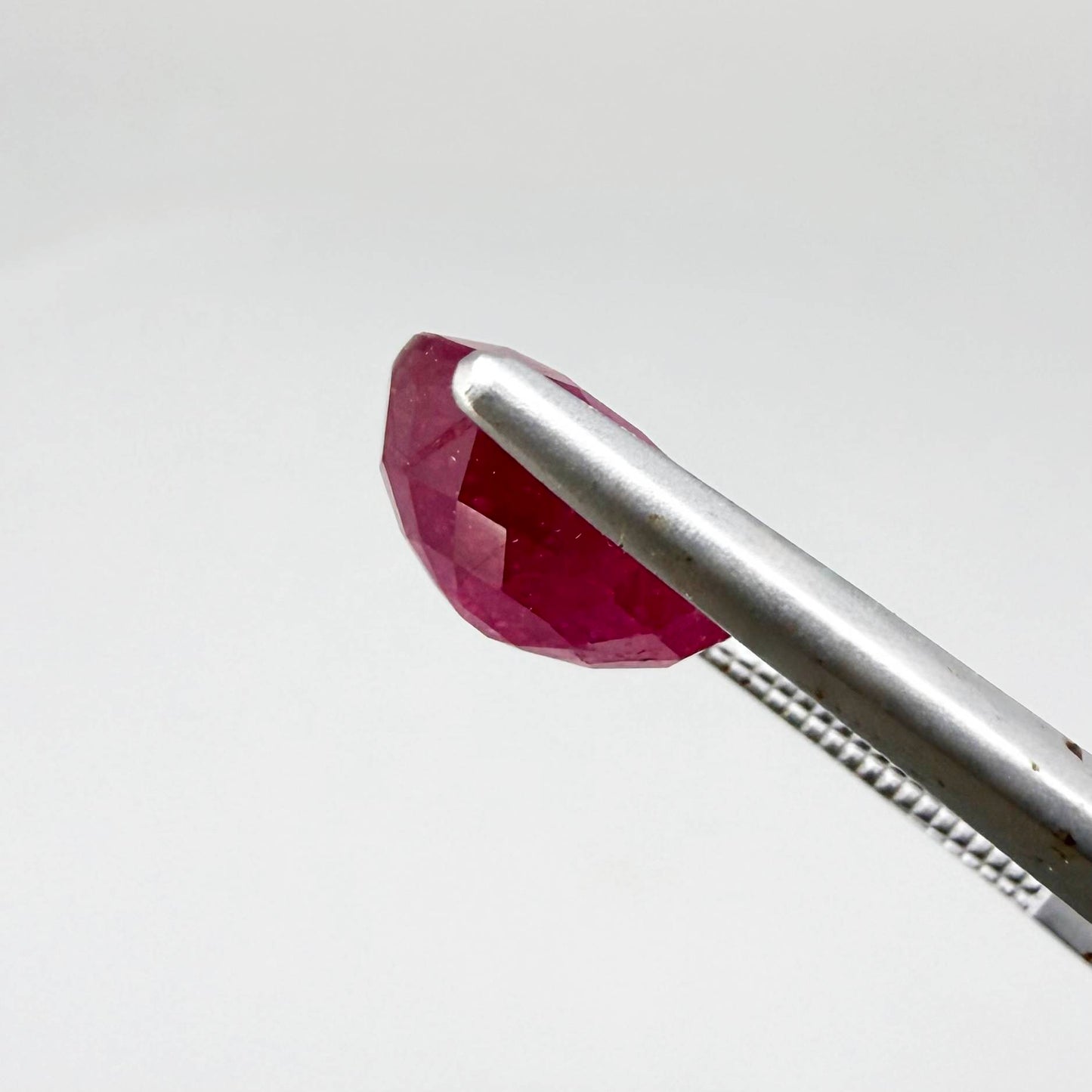 Oval pinkish red ruby from Mozambique with vibrant color, visible natural inclusions and soft, semi-transparent appearance.