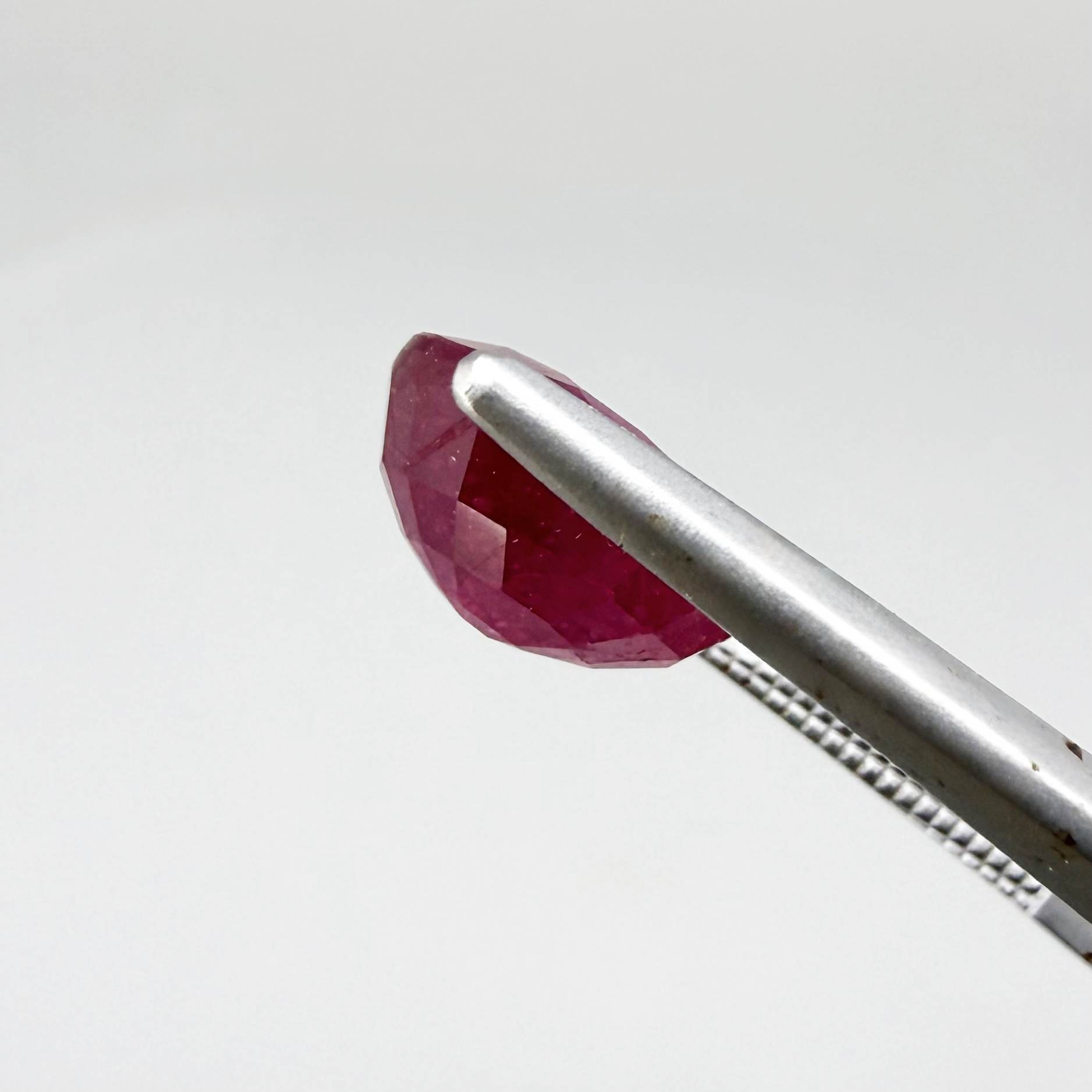 Oval pinkish red ruby from Mozambique with vibrant color, visible natural inclusions and soft, semi-transparent appearance.