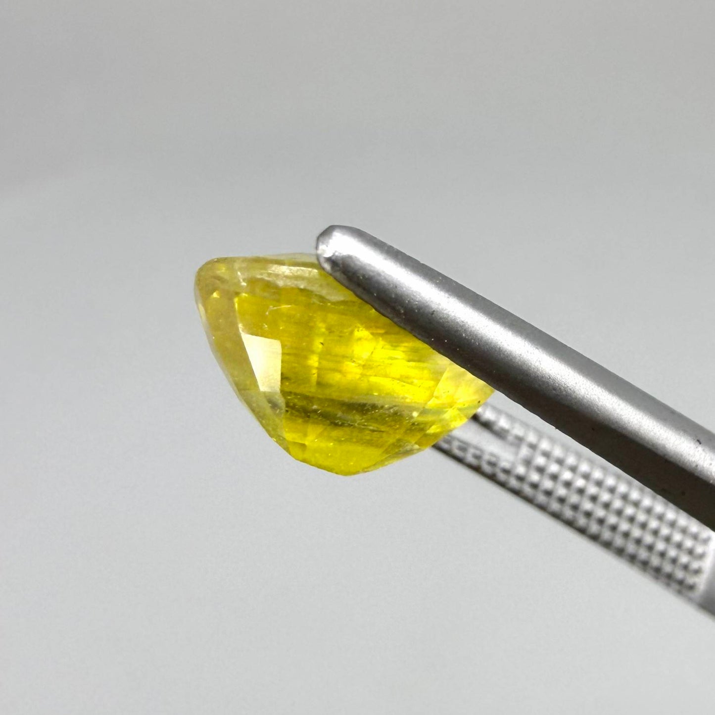 Cushion cut yellow sapphire from Africa,  with vivid golden-yellow color, visible natural inclusions and a transparent to slightly silky structure.