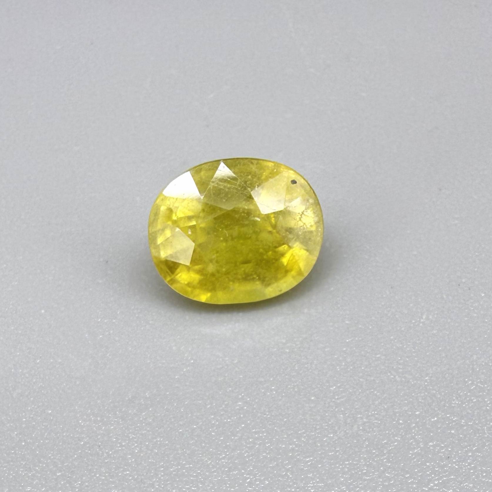 Cushion cut yellow sapphire from Africa,  with vivid golden-yellow color, visible natural inclusions and a transparent to slightly silky structure.