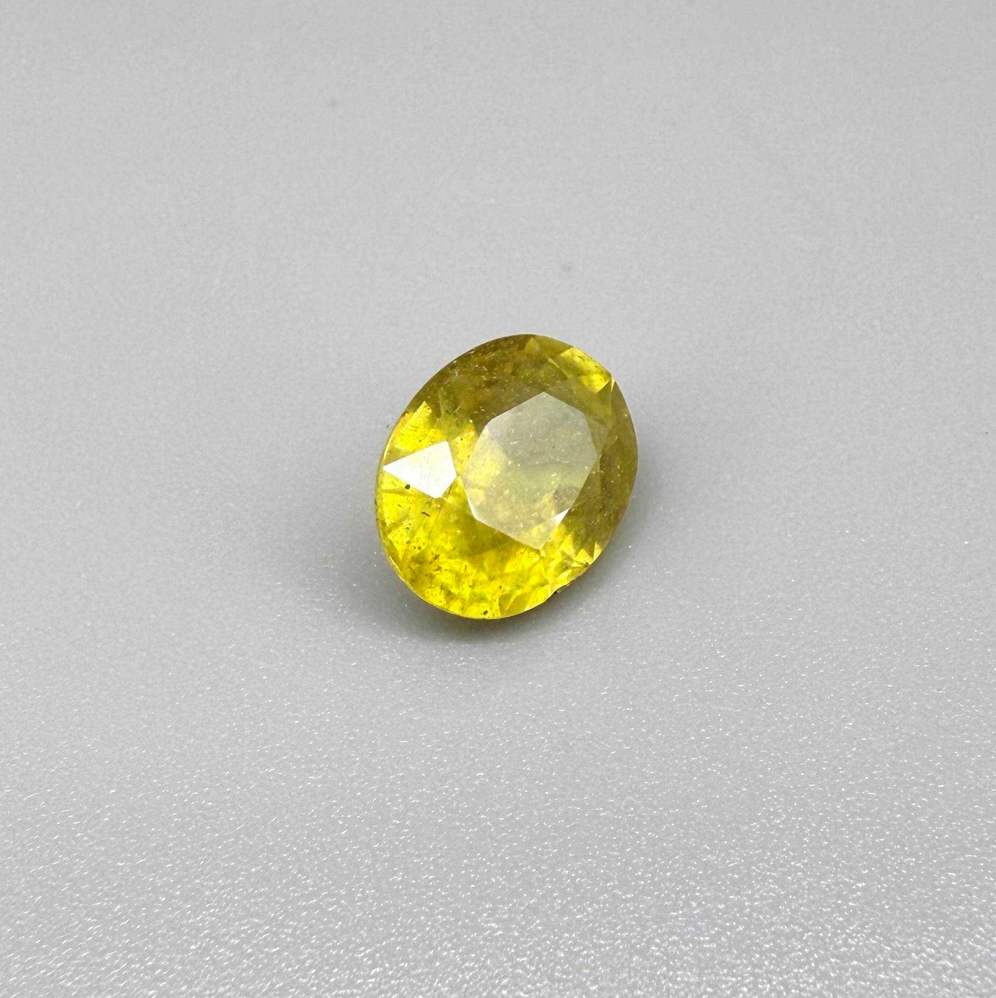 Oval yellow sapphire from Africa, 5.42ct, with vivid golden-yellow color, visible natural inclusions and a transparent to slightly silky appearance.