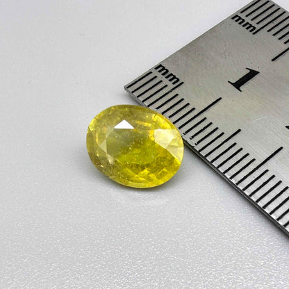 Oval yellow sapphire from Africa, 5.42ct, with vivid golden-yellow color, visible natural inclusions and a transparent to slightly silky appearance.