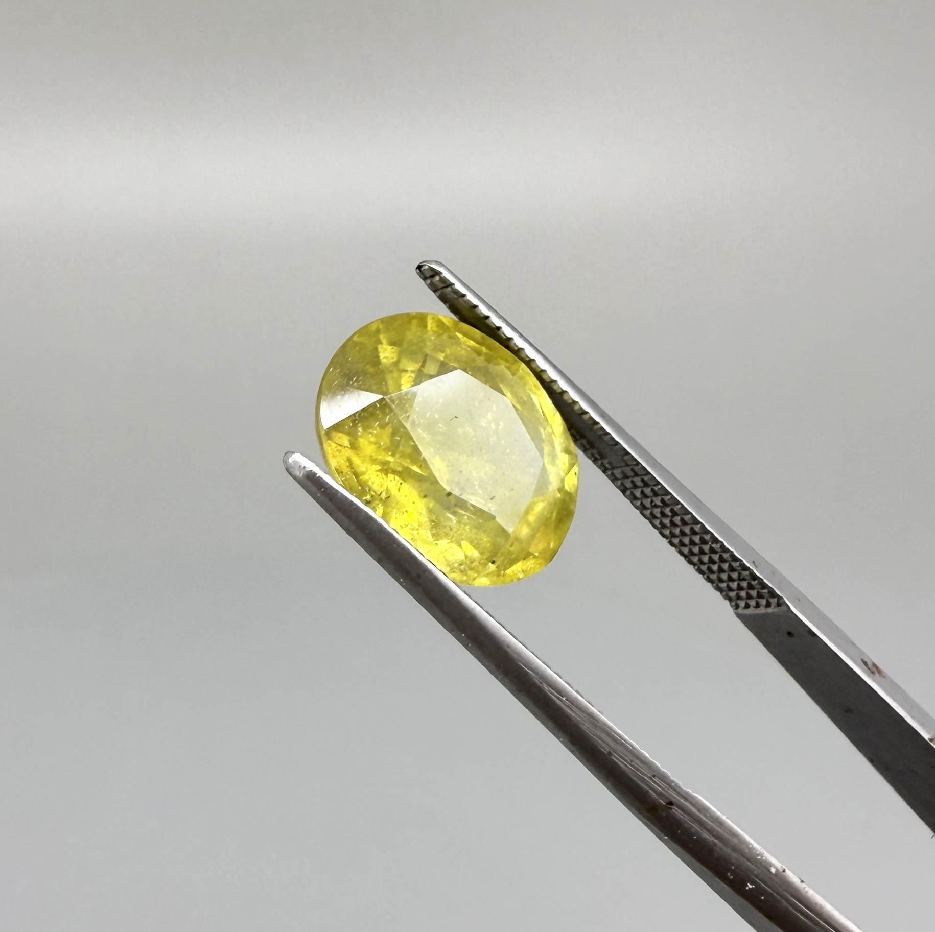 Oval yellow sapphire from Africa, 5.42ct, with vivid golden-yellow color, visible natural inclusions and a transparent to slightly silky appearance.