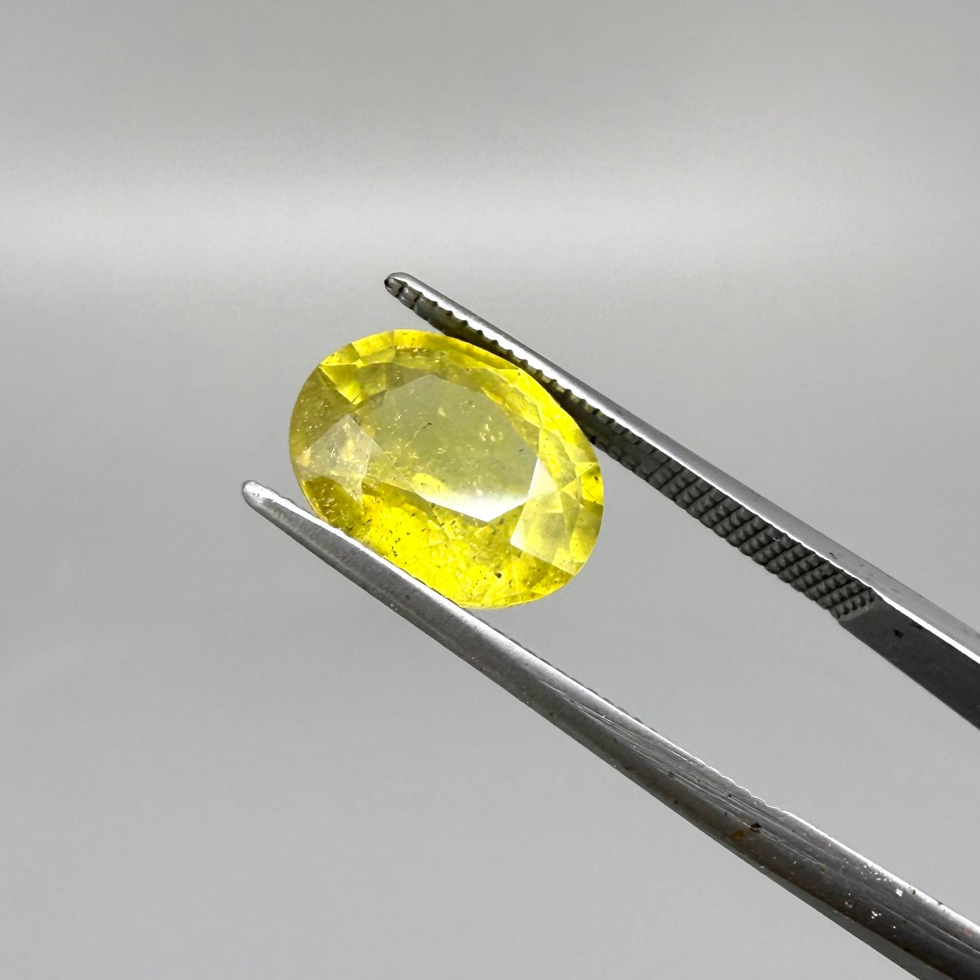 Oval yellow sapphire from Africa, 5.42ct, with vivid golden-yellow color, visible natural inclusions and a transparent to slightly silky appearance.