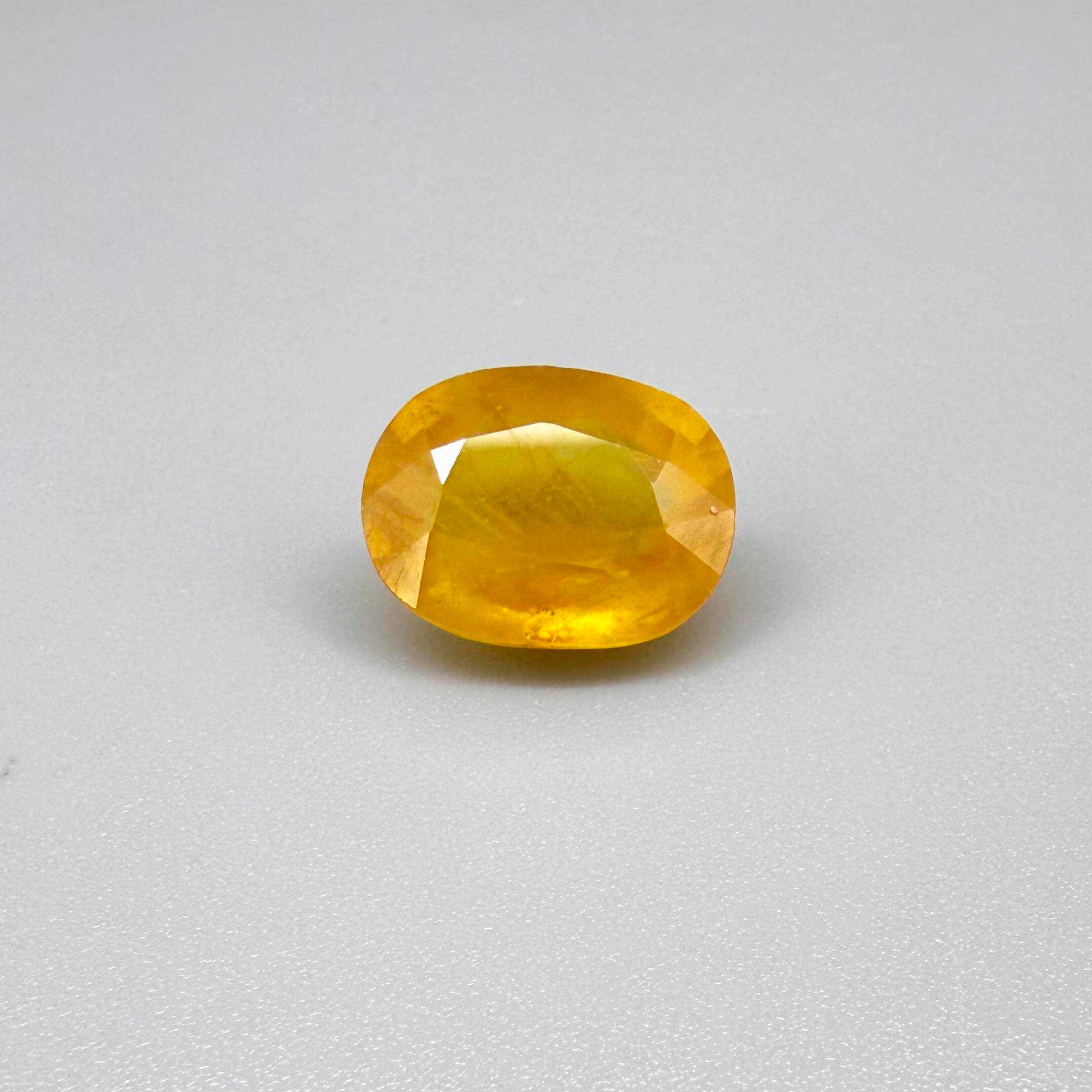Oval orange-yellow sapphire from Africa, with warm golden to orangey color, visible natural inclusions and a transparent to slightly silky appearance.