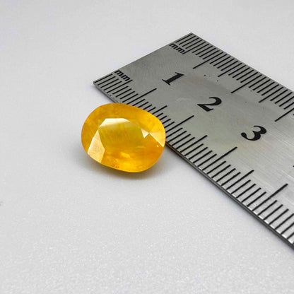 Oval orange-yellow sapphire from Africa, with warm golden to orangey color, visible natural inclusions and a transparent to slightly silky appearance.