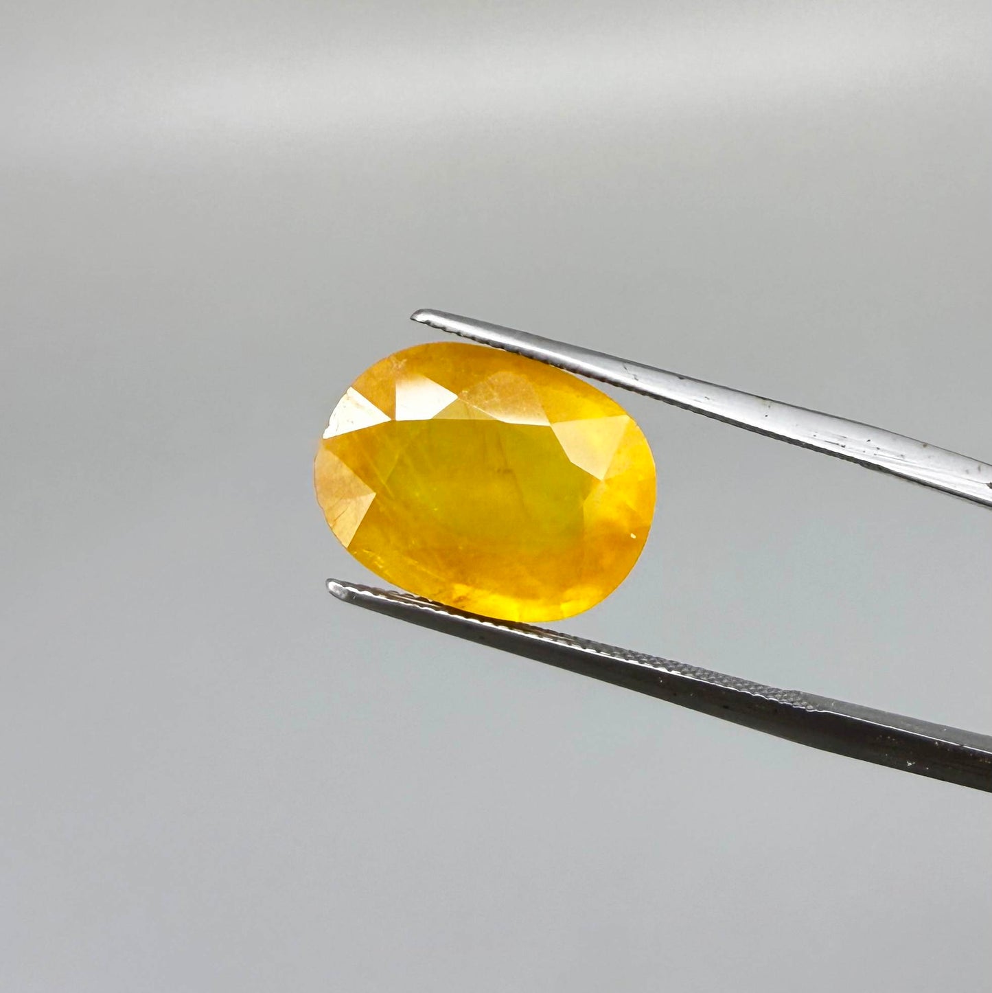 Oval orange-yellow sapphire from Africa, with warm golden to orangey color, visible natural inclusions and a transparent to slightly silky appearance.