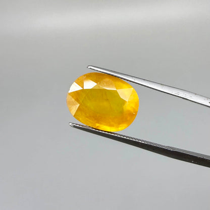 Oval orange-yellow sapphire from Africa, with warm golden to orangey color, visible natural inclusions and a transparent to slightly silky appearance.