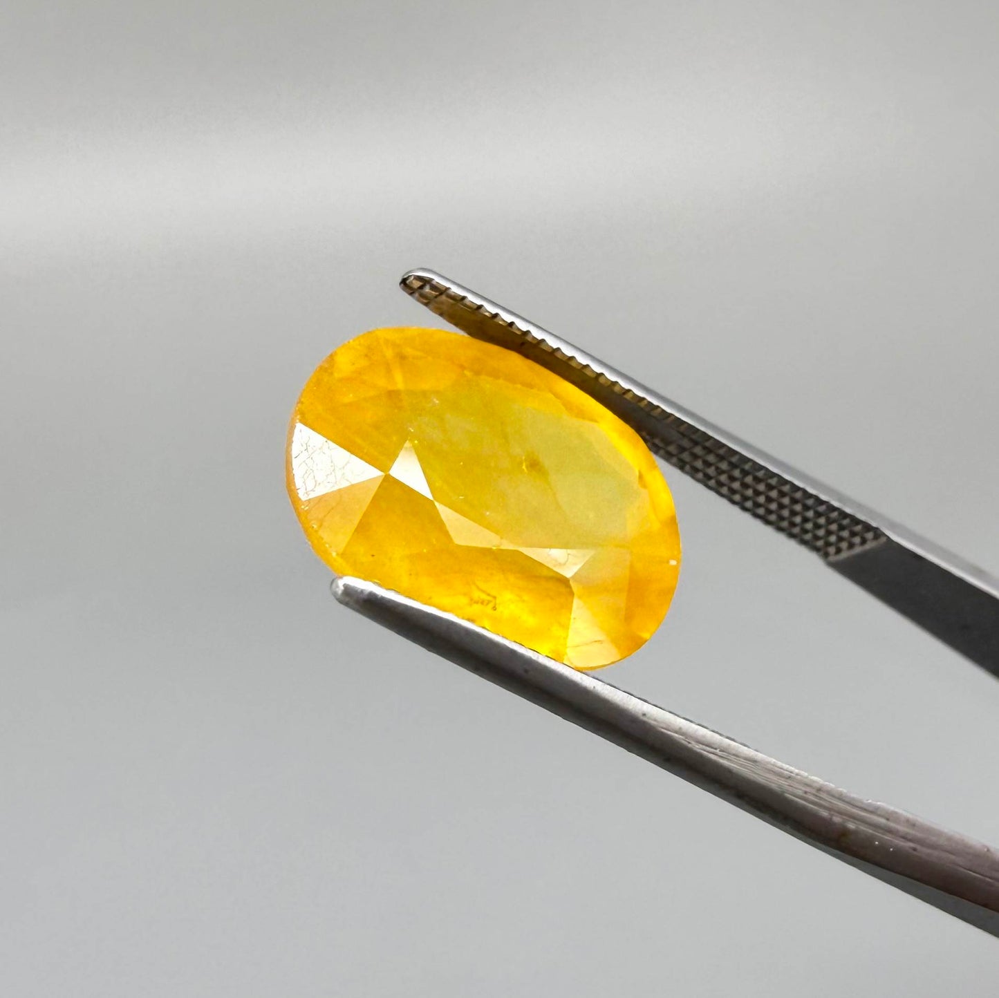 Oval orange-yellow sapphire from Africa, with warm golden to orangey color, visible natural inclusions and a transparent to slightly silky appearance.
