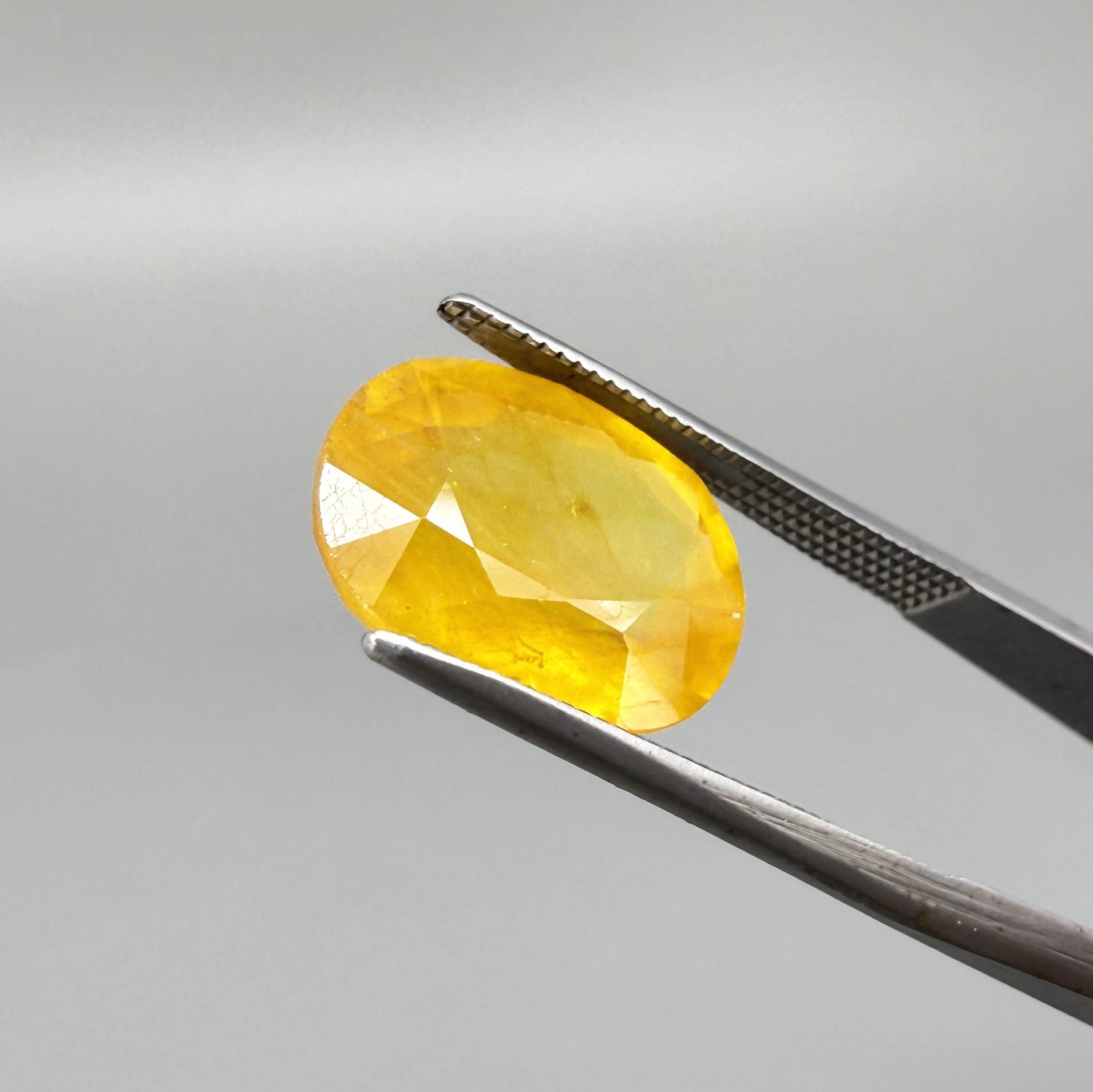 Oval orange-yellow sapphire from Africa, with warm golden to orangey color, visible natural inclusions and a transparent to slightly silky appearance.