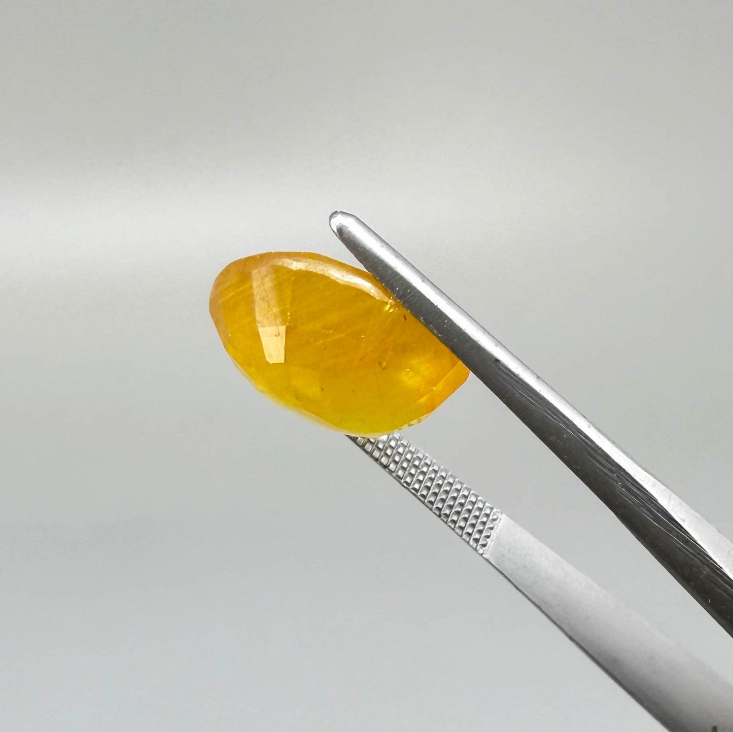 Oval orange-yellow sapphire from Africa, with warm golden to orangey color, visible natural inclusions and a transparent to slightly silky appearance.