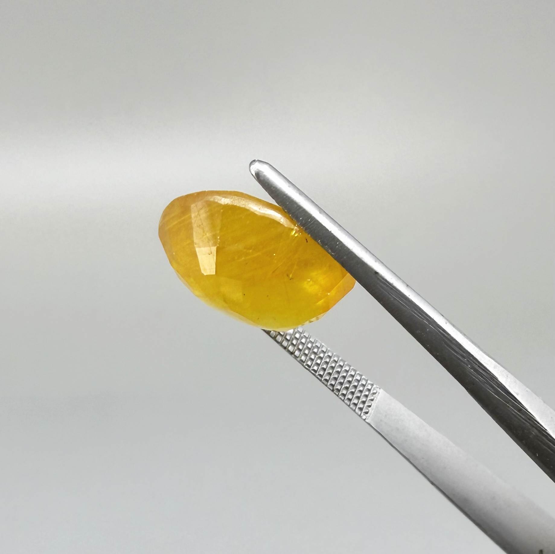 Oval orange-yellow sapphire from Africa, with warm golden to orangey color, visible natural inclusions and a transparent to slightly silky appearance.