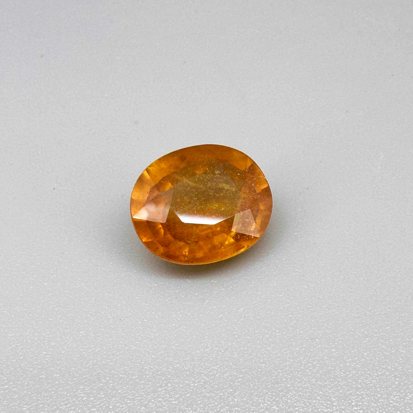 Oval orange sapphire from Africa, 6.04ct, with deep orange to amber color, visible natural inclusions and a transparent to slightly silky appearance.