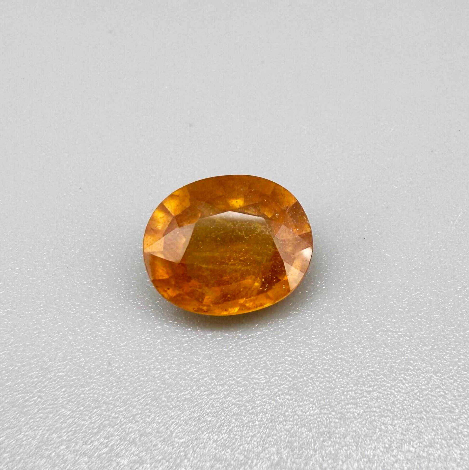 Oval orange sapphire from Africa, 6.04ct, with deep orange to amber color, visible natural inclusions and a transparent to slightly silky appearance.