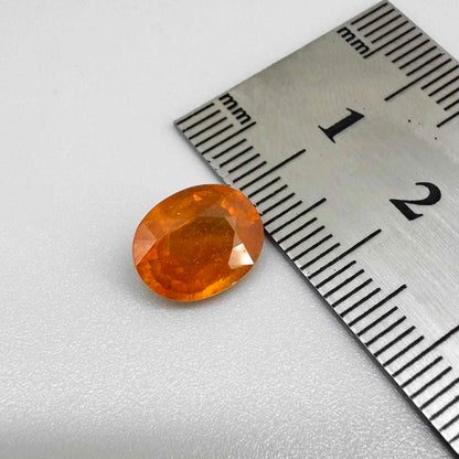 Oval orange sapphire from Africa, 4.43ct, with deep burnt orange color, visible natural inclusions and a transparent to slightly silky appearance.