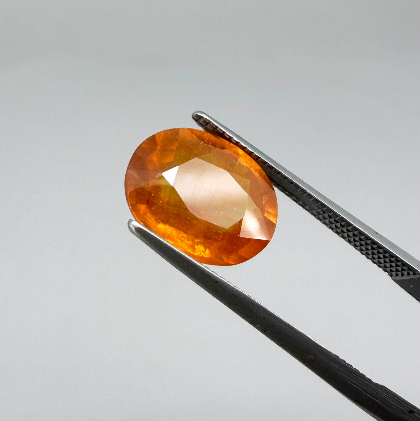 Oval orange sapphire from Africa, 4.43ct, with deep burnt orange color, visible natural inclusions and a transparent to slightly silky appearance.
