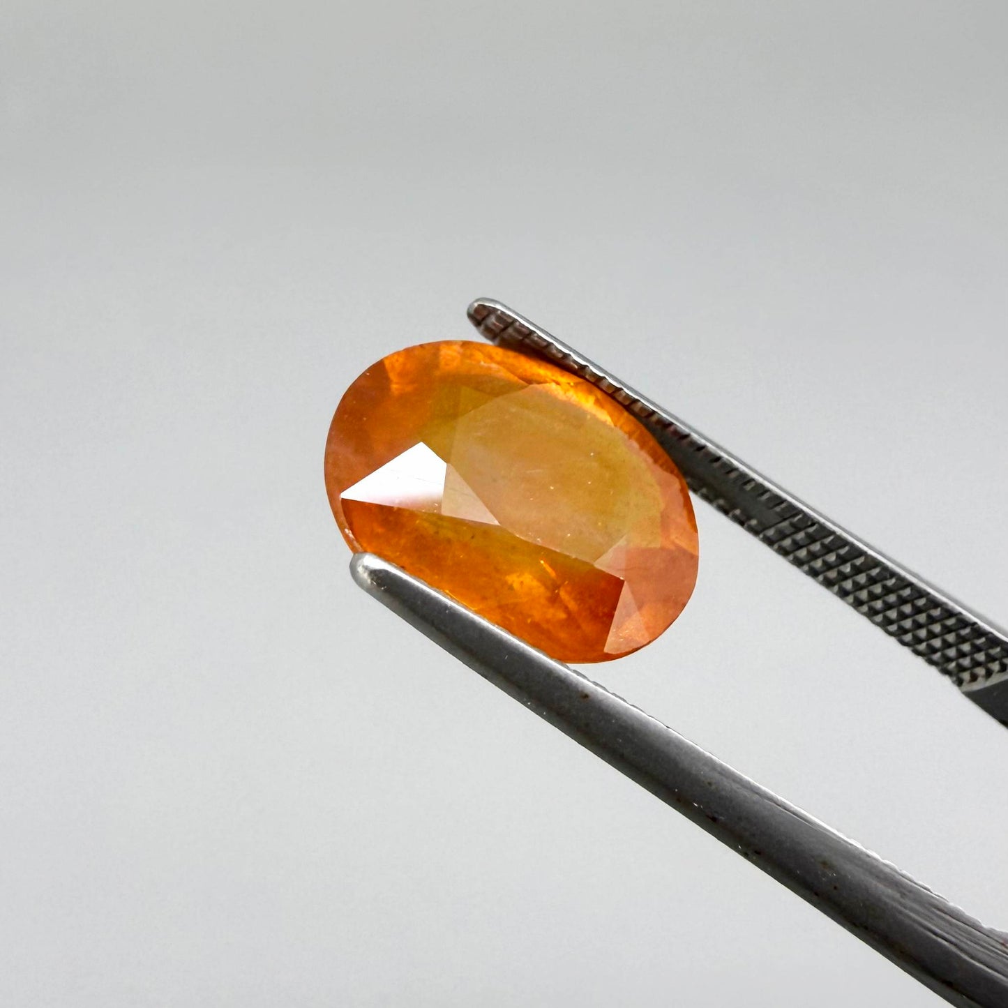 Oval orange sapphire from Africa, 4.43ct, with deep burnt orange color, visible natural inclusions and a transparent to slightly silky appearance.