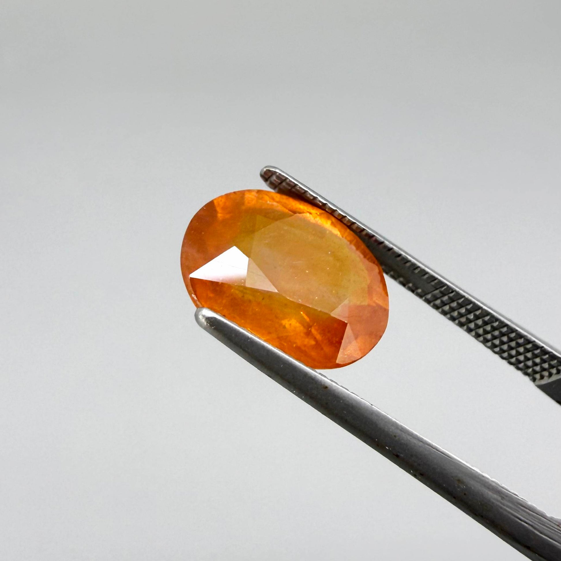 Oval orange sapphire from Africa, 4.43ct, with deep burnt orange color, visible natural inclusions and a transparent to slightly silky appearance.