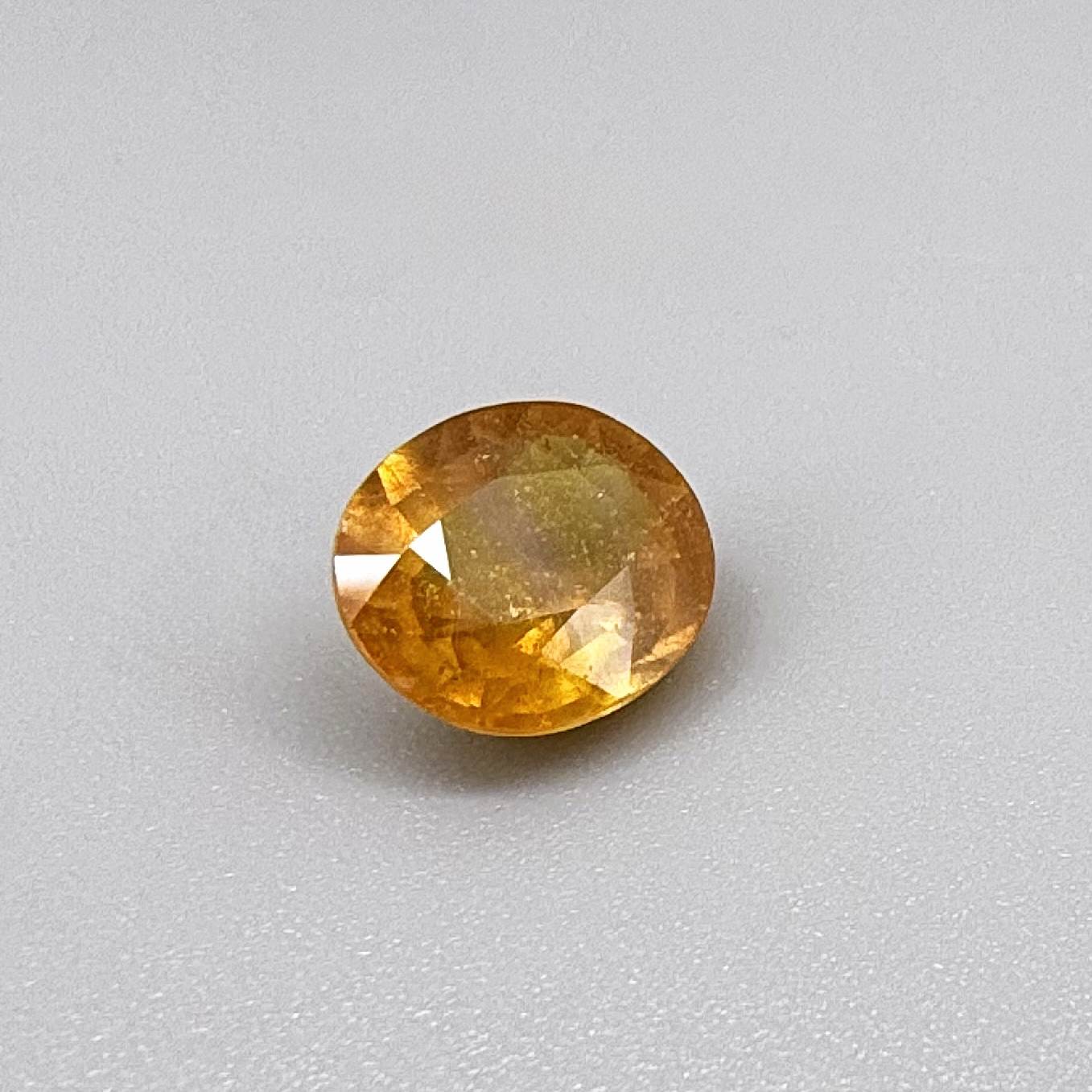 Oval yellow to orange sapphire from Africa, 5.47ct, with bright golden color and slight orangey tones, visible natural inclusions and a transparent to slightly silky appearance.