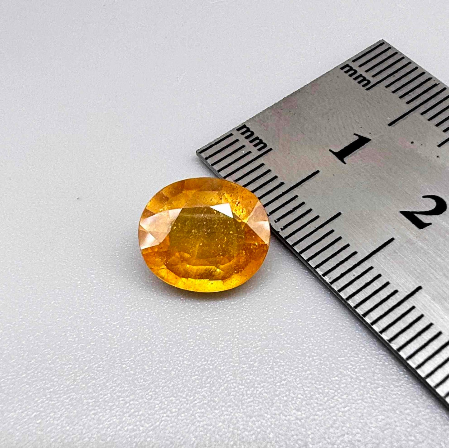 Oval yellow to orange sapphire from Africa, 5.47ct, with bright golden color and slight orangey tones, visible natural inclusions and a transparent to slightly silky appearance.