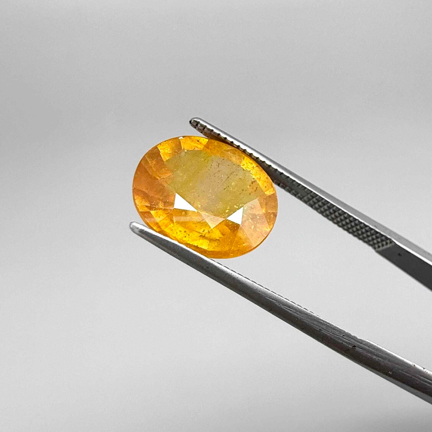 Oval yellow to orange sapphire from Africa, 5.47ct, with bright golden color and slight orangey tones, visible natural inclusions and a transparent to slightly silky appearance.