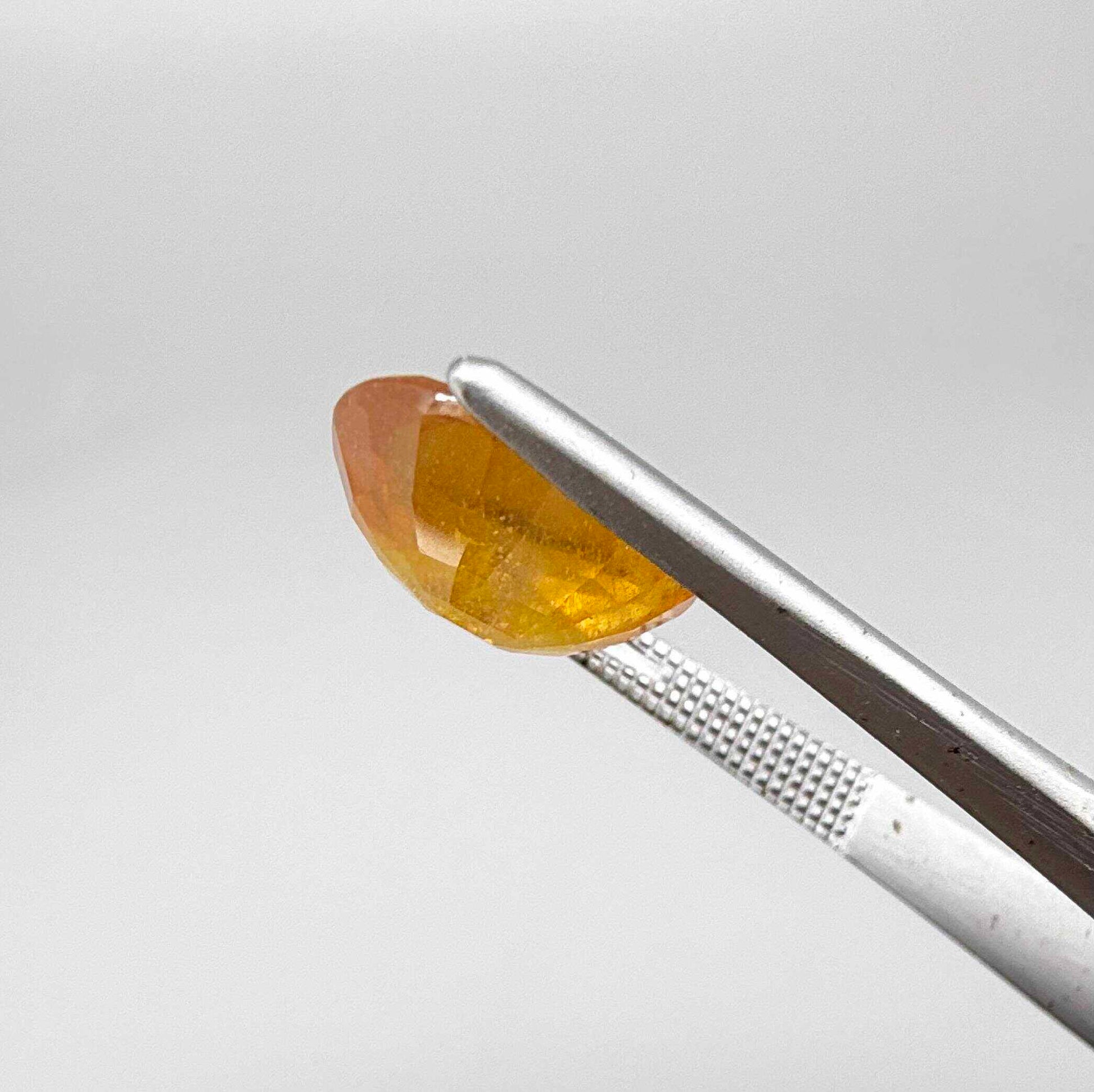 Oval yellow to orange sapphire from Africa, 5.47ct, with bright golden color and slight orangey tones, visible natural inclusions and a transparent to slightly silky appearance.