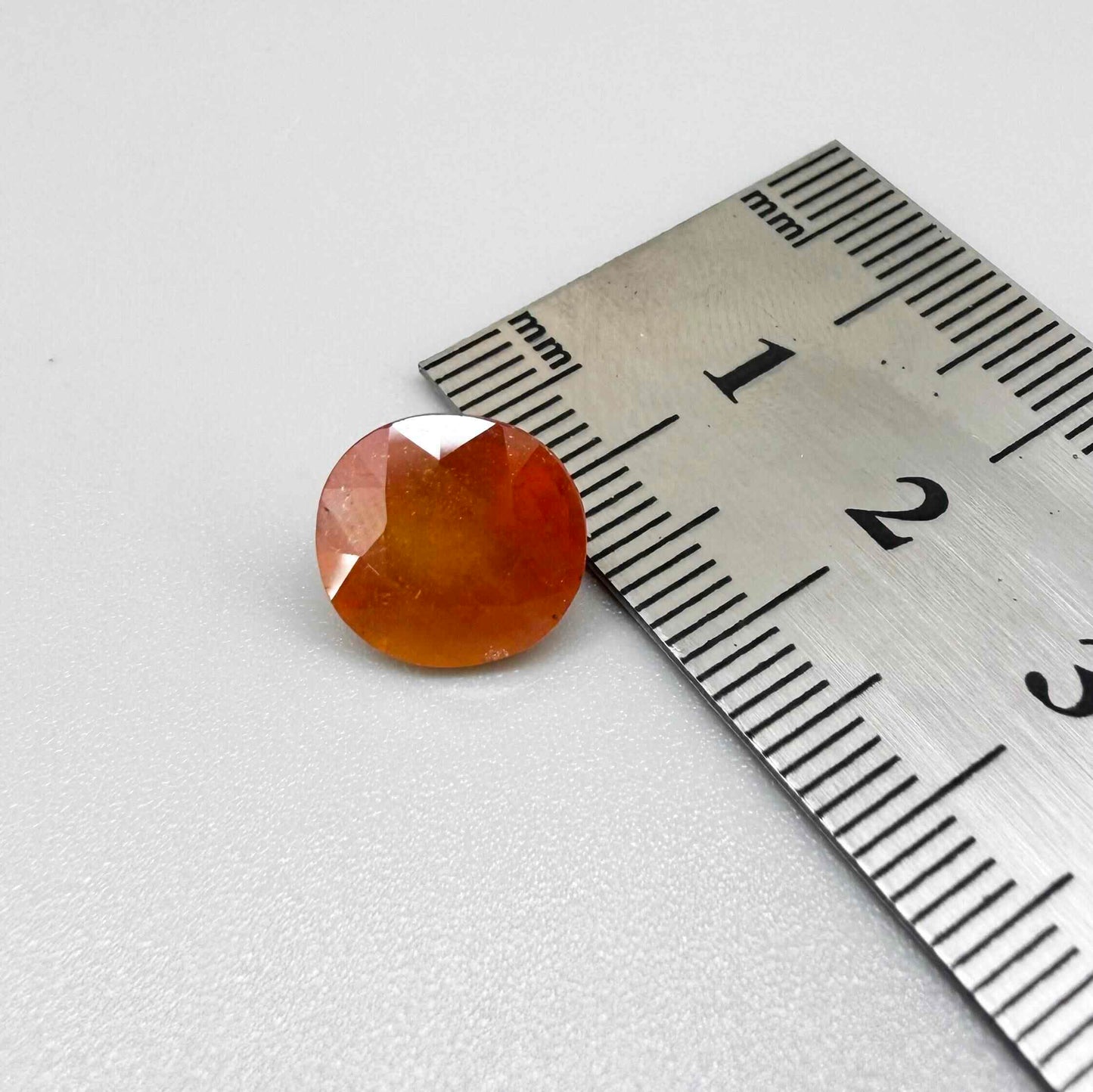 Oval orange sapphire from Africa, 6.2ct, with vivid orange color and a lighter yellowish center, visible natural inclusions and a transparent to slightly silky appearance.