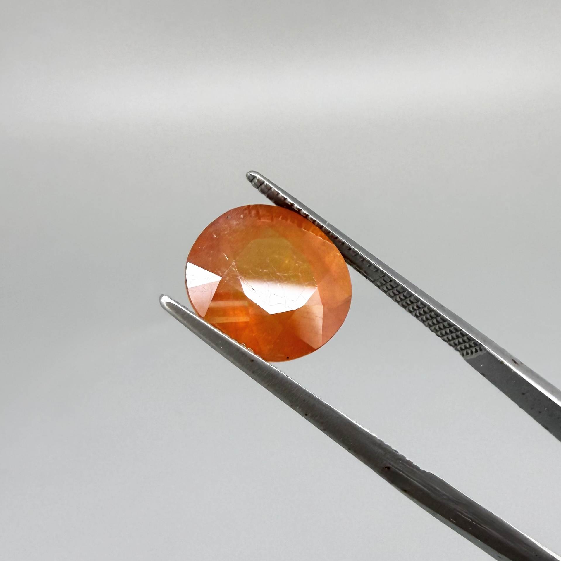 Oval orange sapphire from Africa, 6.2ct, with vivid orange color and a lighter yellowish center, visible natural inclusions and a transparent to slightly silky appearance.
