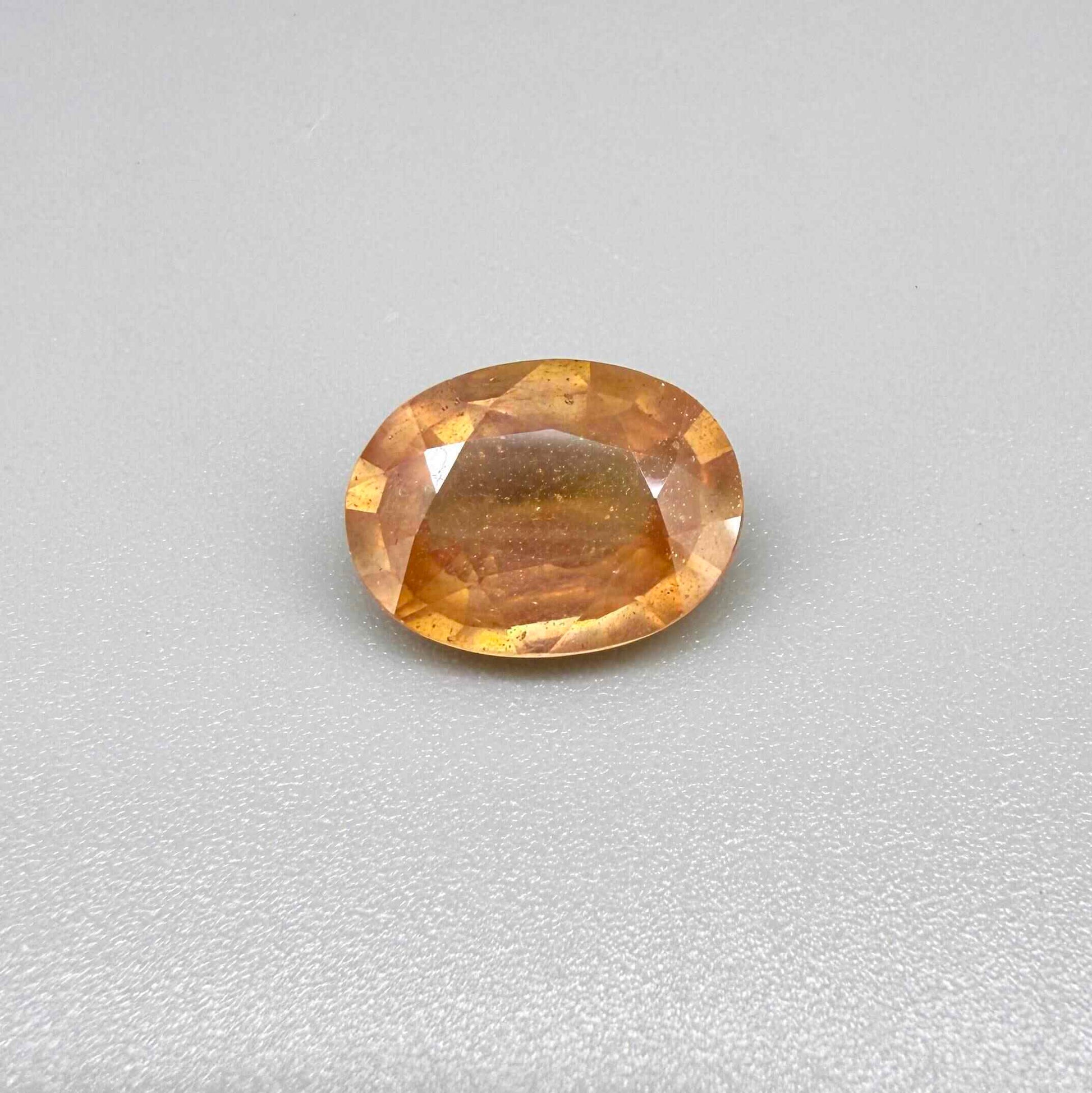 Oval peach to light orange sapphire from Africa, 6.3ct, with soft pastel tones, visible natural inclusions and a transparent to slightly silky appearance.