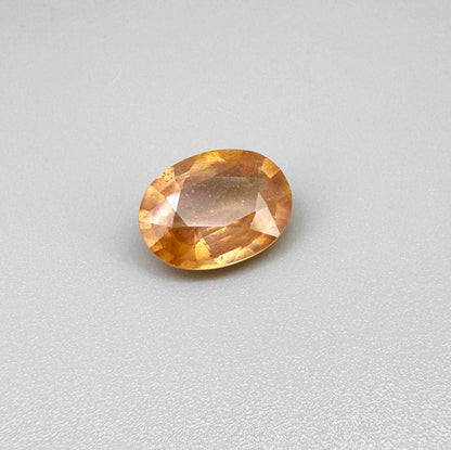 Oval peach to light orange sapphire from Africa, 6.3ct, with soft pastel tones, visible natural inclusions and a transparent to slightly silky appearance.