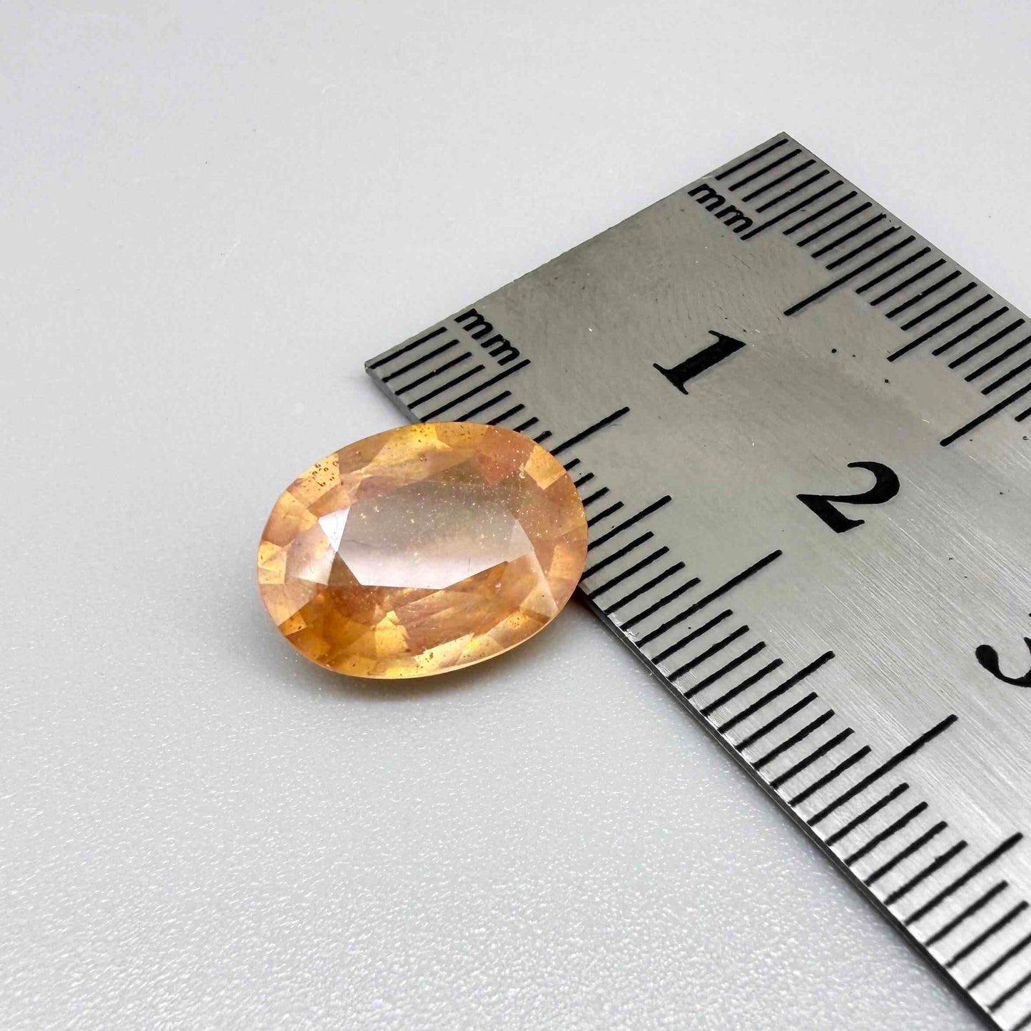 Oval peach to light orange sapphire from Africa, 6.3ct, with soft pastel tones, visible natural inclusions and a transparent to slightly silky appearance.