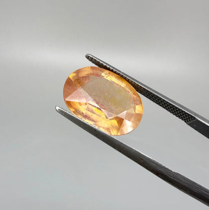 Oval peach to light orange sapphire from Africa, 6.3ct, with soft pastel tones, visible natural inclusions and a transparent to slightly silky appearance.