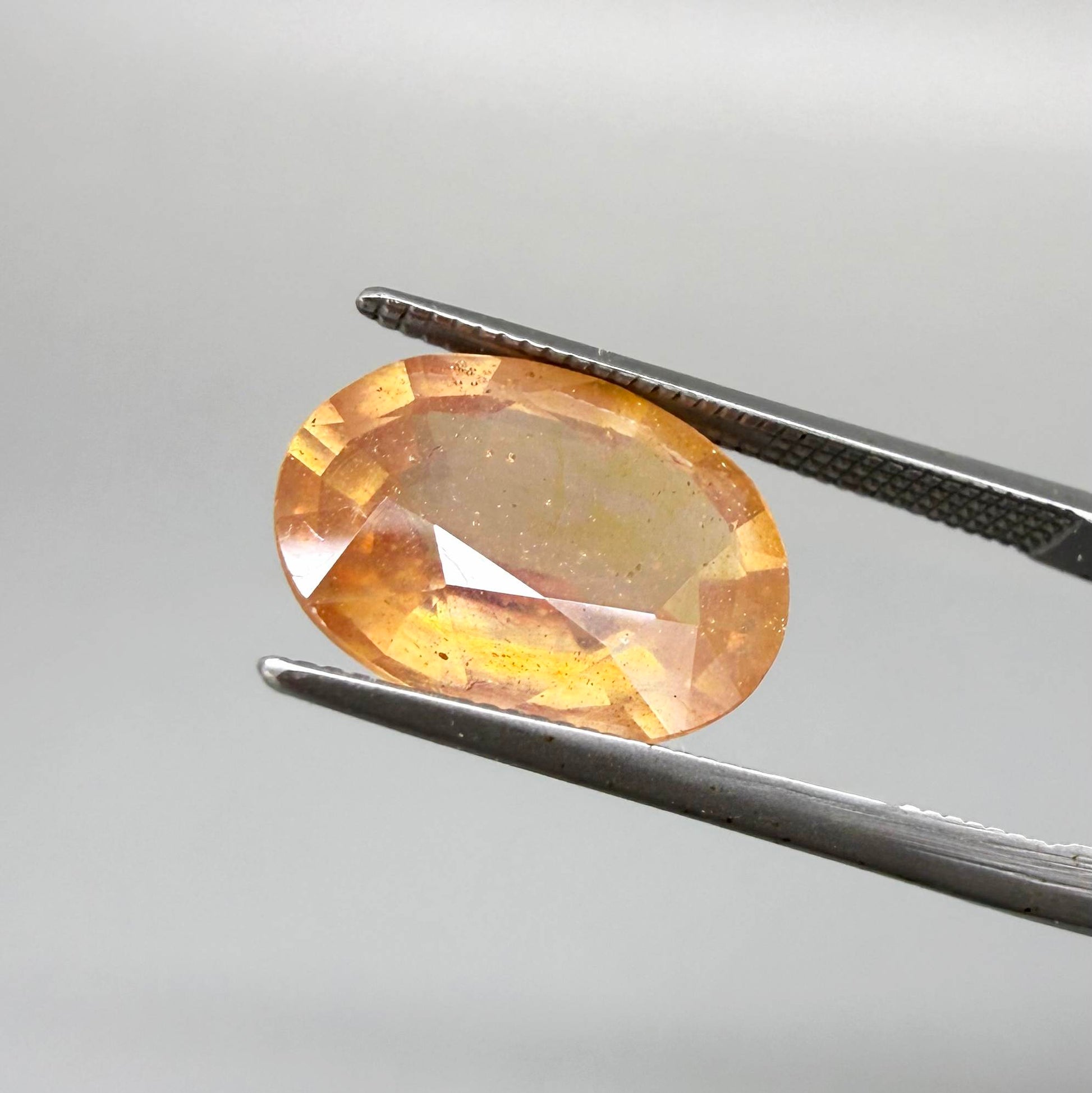 Oval peach to light orange sapphire from Africa, 6.3ct, with soft pastel tones, visible natural inclusions and a transparent to slightly silky appearance.