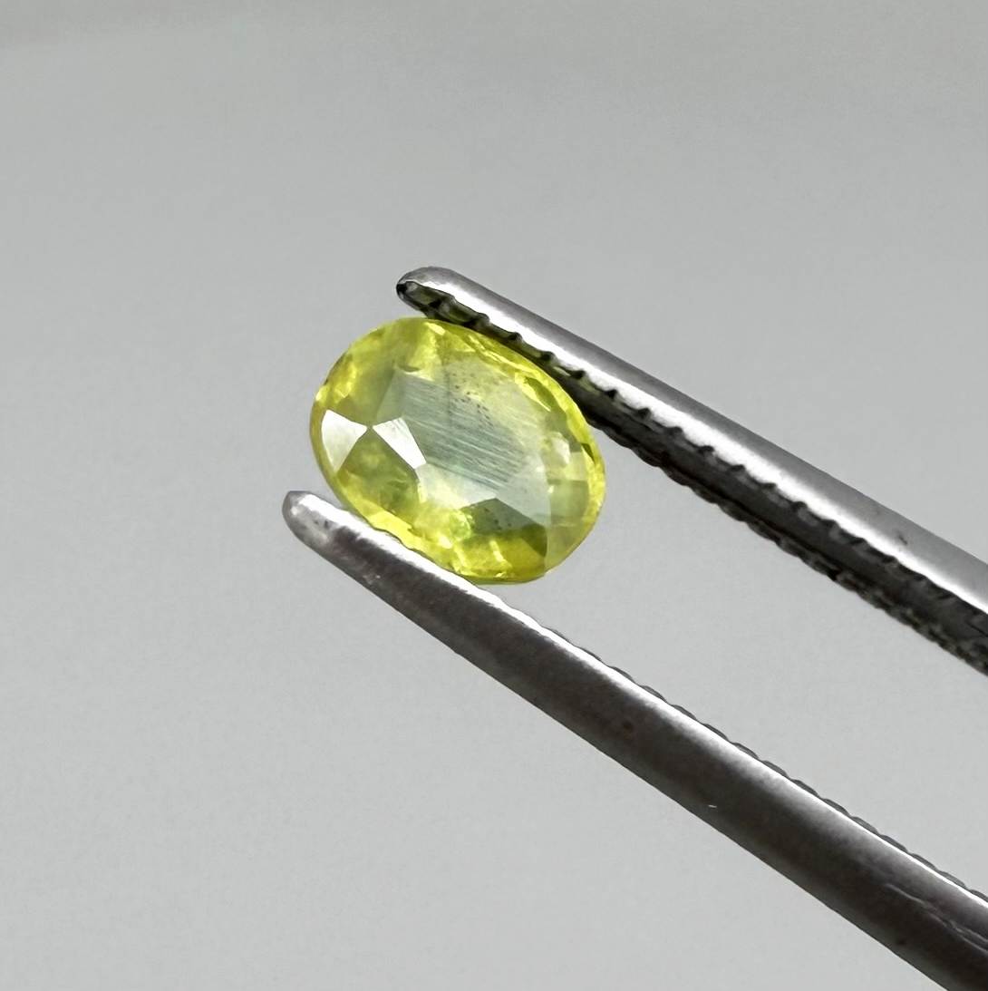 Oval greenish yellow sapphire from Thailand, 0.35ct, unheated, with bright yellow-dominant color and green undertones, visible natural inclusions and a transparent to slightly silky appearance.