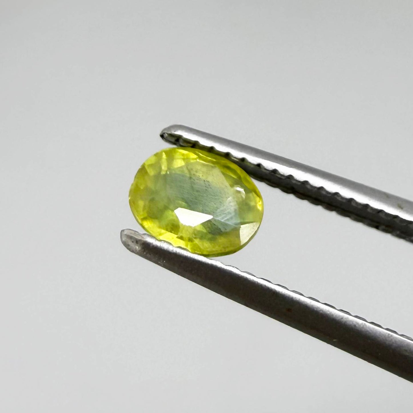 Oval greenish yellow sapphire from Thailand, 0.35ct, unheated, with bright yellow-dominant color and green undertones, visible natural inclusions and a transparent to slightly silky appearance.
