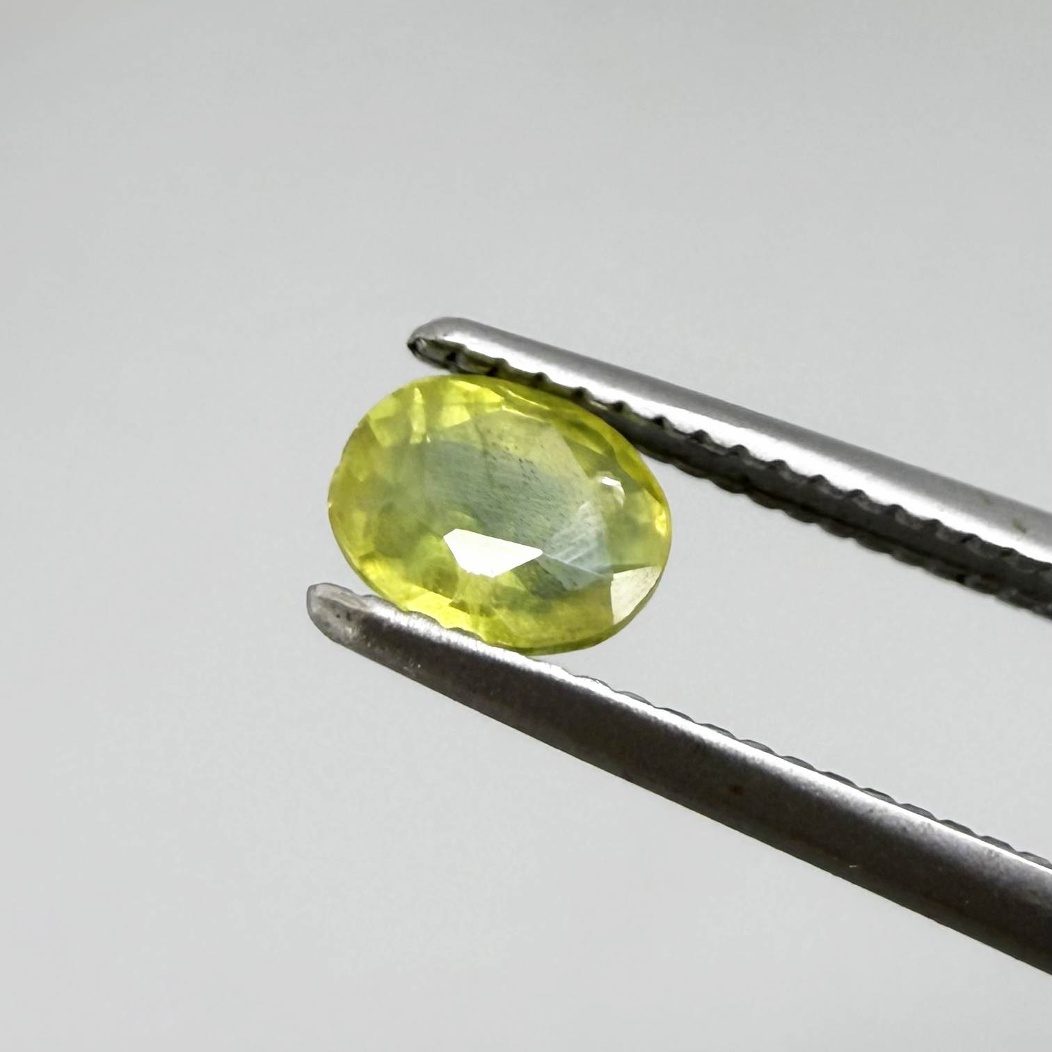 Oval greenish yellow sapphire from Thailand, 0.35ct, unheated, with bright yellow-dominant color and green undertones, visible natural inclusions and a transparent to slightly silky appearance.