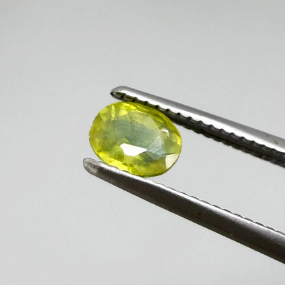 Oval greenish yellow sapphire from Thailand, 0.35ct, unheated, with bright yellow-dominant color and green undertones, visible natural inclusions and a transparent to slightly silky appearance.