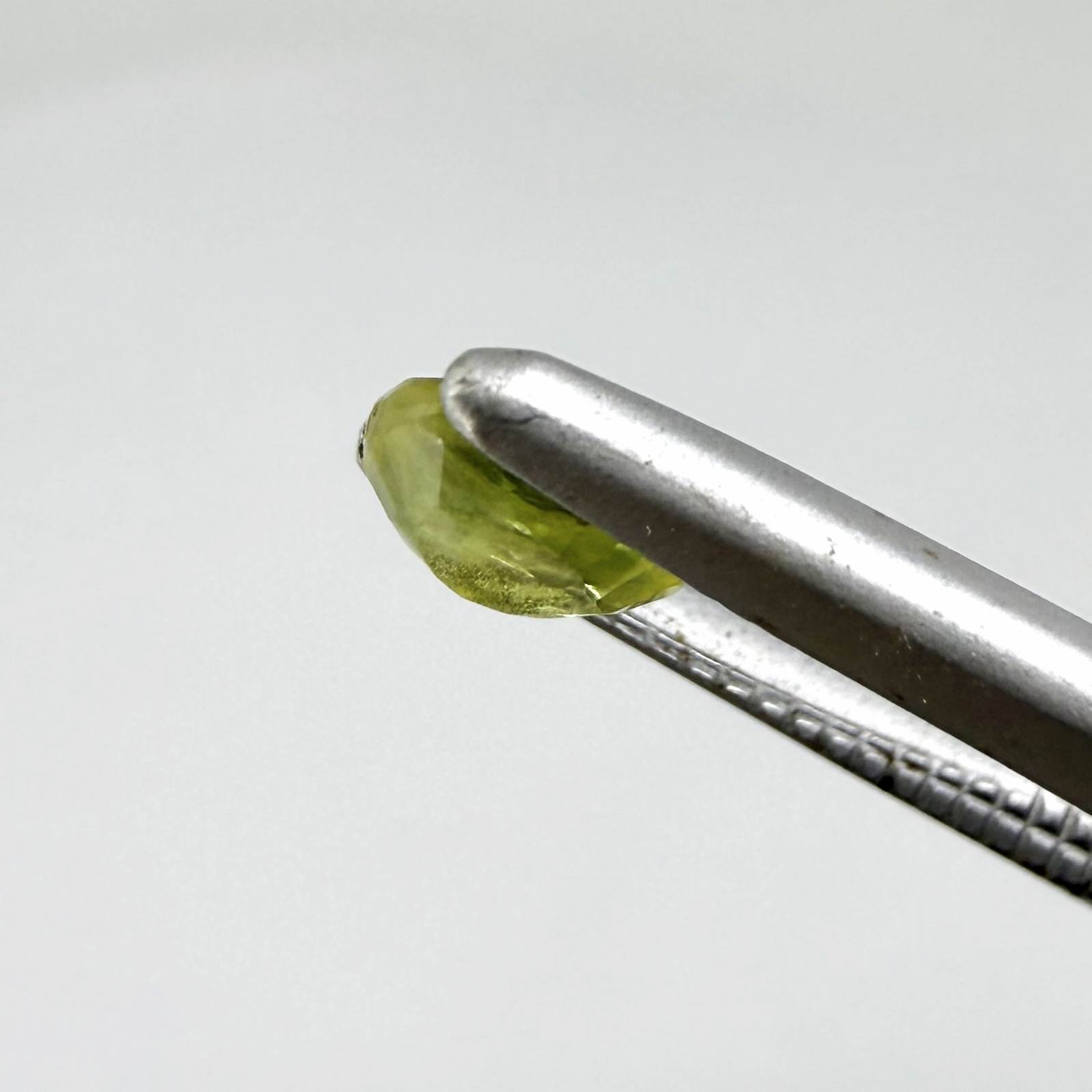 Oval greenish yellow sapphire from Thailand, 0.35ct, unheated, with bright yellow-dominant color and green undertones, visible natural inclusions and a transparent to slightly silky appearance.