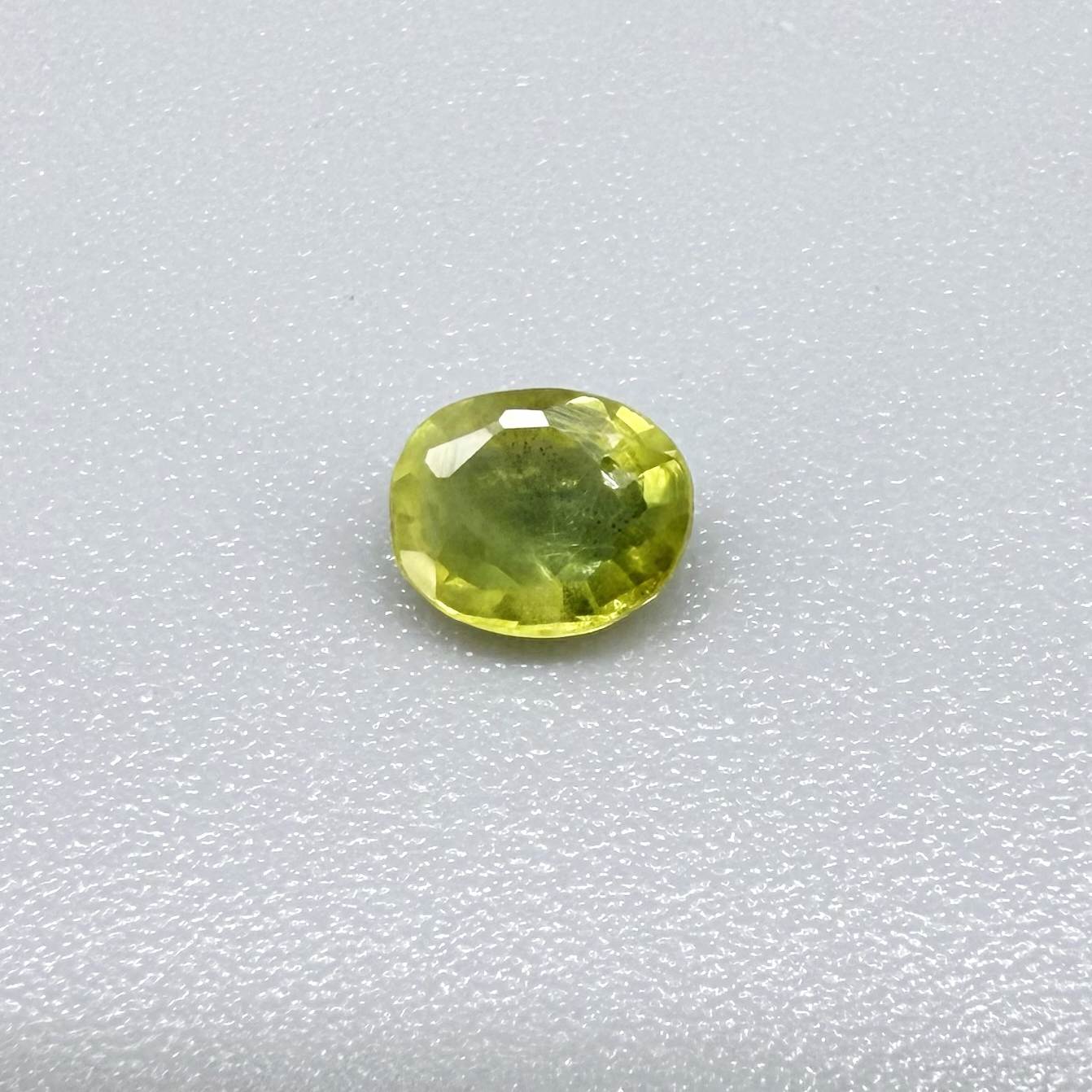 Oval greenish yellow sapphire from Thailand, 0.35ct, unheated, with bright yellow-dominant color and green undertones, visible natural inclusions and a transparent to slightly silky appearance.